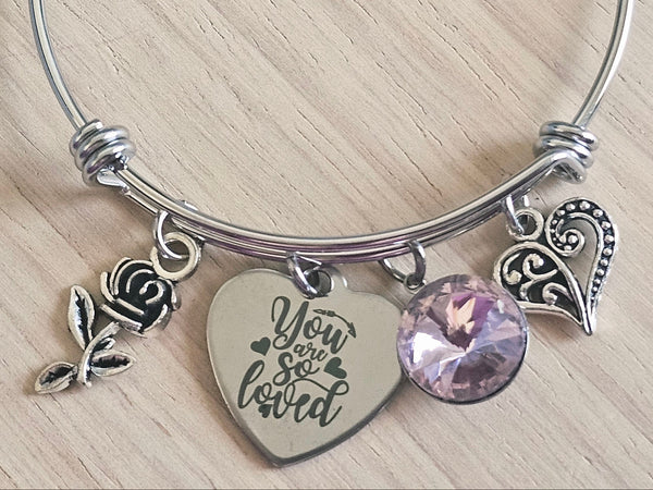 Silver bracelet with heart-shaped charm and purple heart charm on a light wooden surface